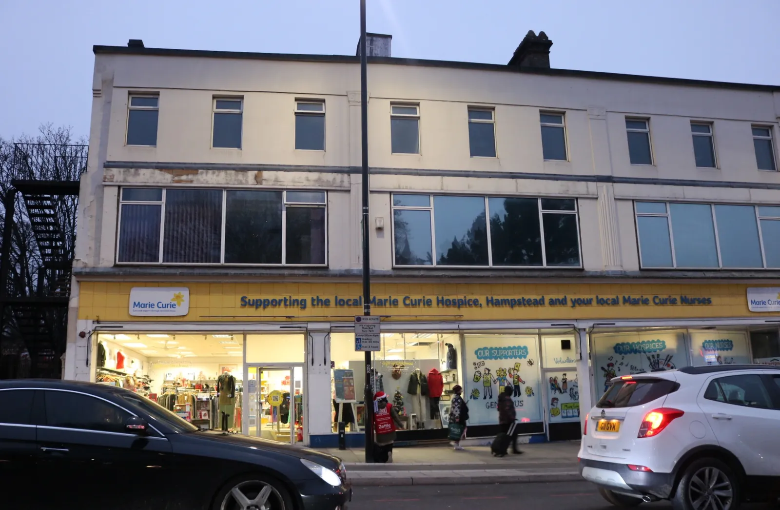 The long front of a Marie Curie charity shop at Highbury Corner, with rails visible through the windows