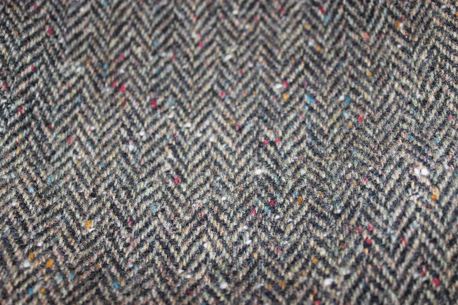 Close-up of a herringbone tweed in brown and black, flecked with red, blue and white