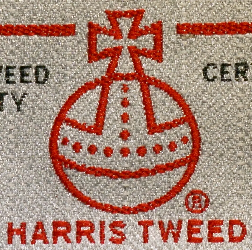 A red Harris Tweed orb label woven into a grey cloth tag